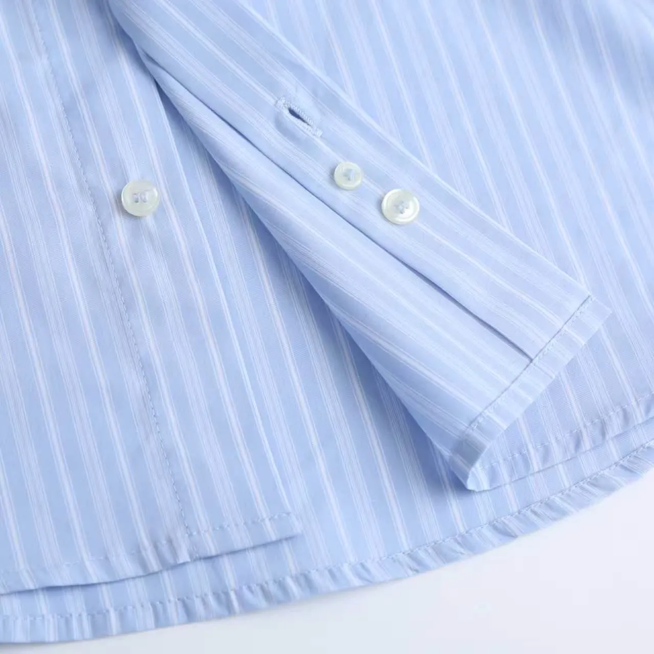 AMI Embroidered Striped Shirt Fabric Selection: Made of 100% cotton poplin fabric. The pure cotton fiber can quickly absorb moisture and perspire, making it refreshing and not stuffy when worn for a long time. The unique plain weave process of poplin makes the fabric both soft and skeletal, not easy to wrinkle and deform, and the upper body is neat and clean. Coupled with the fine blue and white stripes all over the body, the light color scheme is gentle and elegant, which can meet the needs of different scenes. Process 1: Accurately mark the embroidery position on the chest patch pocket to ensure that the pattern does not shift and does not destroy the overall beauty of the striped fabric. High-count embroidery threads of the same color as the fabric are selected, and flat stitch embroidery technology is used. The stitches are evenly tracked, the edges are clean and neat, and the love outline is simple and smooth. It retains recognition without irritating the skin. It is blended into the striped texture in a low-key manner to avoid an abrupt feeling, while ensuring that the embroidery threads are Wear-Resistant. 2: After the embroidery is completed, perform high-temperature ironing and thread trimming to ensure that the pattern is smooth and compliant, and it is not easy to lose thread or warp after being worn for a long time. Details: 1. The collar seat adopts double-layer reinforcement technology, which is not easy to collapse and deform after long-term wear. The collar corner has a soft arc, which can modify the neck line without being too sharp, making it neat and decent. 2. The inner side of the placket has hidden hemming treatment to avoid burrs on the fabric, while enhancing structural stability and preventing it from deforming after multiple washes. Accessories: One-to-one customized buttons Size: S M L XL Style number: D 236